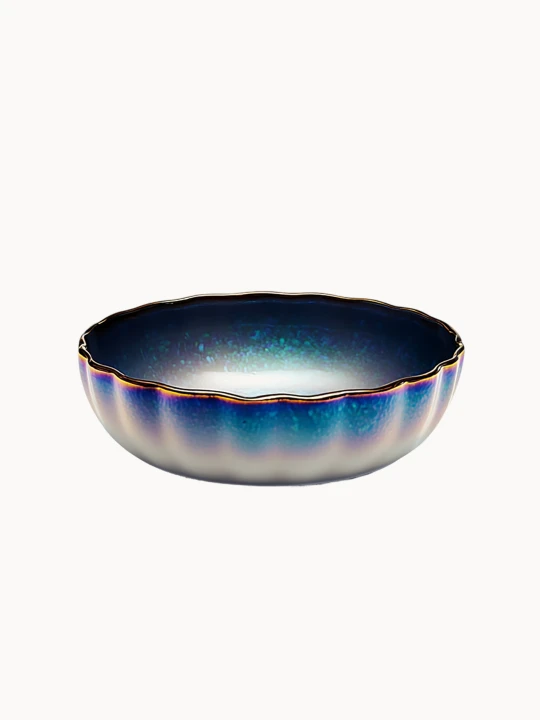 Okrągła ceramiczna miska o karbowanej strukturze, pokryta iryzującym, mieniącym się szkliwem z gradientem od głębokiego metalicznego błękitu do bieli. Artystyczne naczynie wieńczy delikatny, złoty i pofalowany rant.