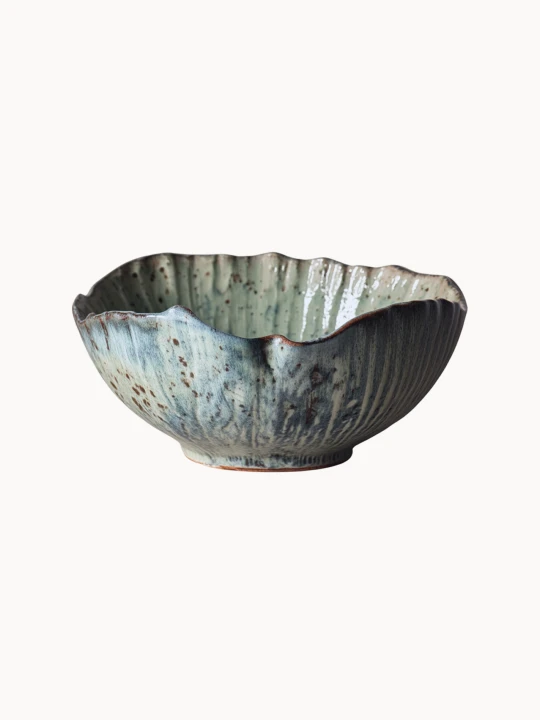 Rustykalna ceramiczna miska pokryta melanżowym jasnoniebieskim i beżowym szkliwem z brązowymi, nakrapianymi detalami na jednolitym białym tle.